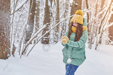 穿着编织帽子的漂亮年轻女孩在森林中的雪中玩耍图片