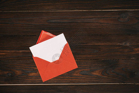 红色信封顶上木制表格上有空白纸背景图片