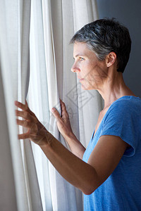 老妇人拉开窗帘望向窗外的肖像背景图片