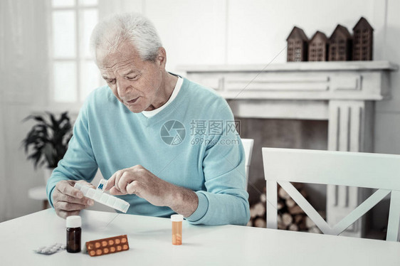 有帮助的药物年长有兴趣的重男坐在桌子边坐着拿着一包平图片