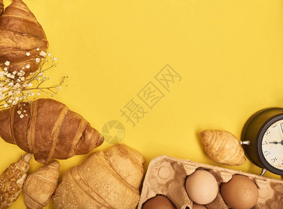 黄色背景的新鲜烘烤美味羊角面包鸡蛋警铃木头和花朵的近视图图片