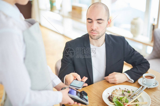 现代商人在咖啡馆的付款终端持有智能手机图片