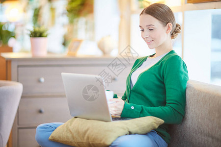青年妇女用笔记本电脑和茶杯坐在沙图片