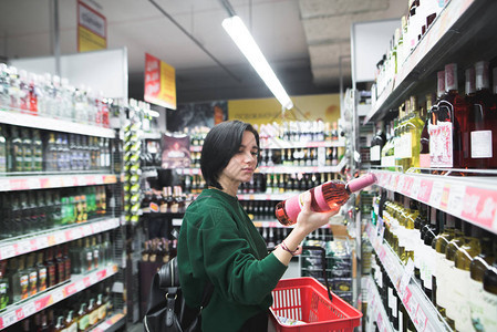 一个漂亮的女孩在超市购物时仔细地看着酒瓶这个女孩读了一个酒标图片