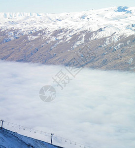 缆车从雾谷中升起缆车是空的背景是被雪覆盖的山脉天空是蓝色图片