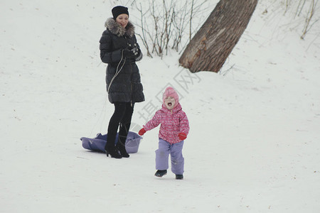 妈让他不听话的女儿坐在冬季街上的雪橇上图片