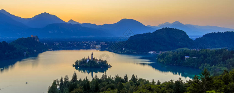 清晨时日在朱利安阿尔卑斯山上空与岛屿上著名的地标教堂相交的湖泊Ble图片