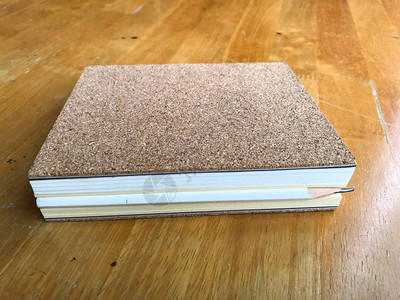 在木本上用软木制成的笔记本之间白色铅笔图片
