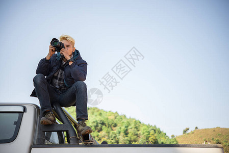 年轻摄影师坐在小卡车上拍摄山上照片背景图片