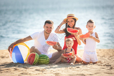 年轻的父母带着孩子在海滩上吃西瓜图片