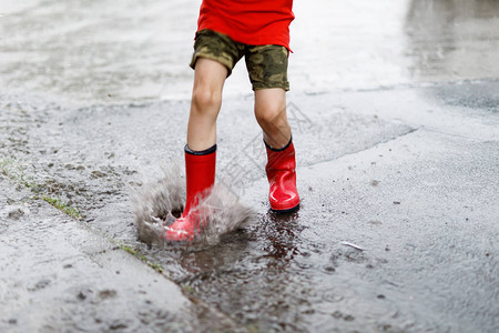 穿着红色雨靴的孩子跳进水坑特写孩子玩得开心泼水温暖的夏雨图片