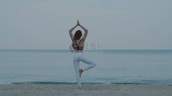 美丽的年轻女孩在海边和天空背景的沙滩上每天早上练瑜伽图片