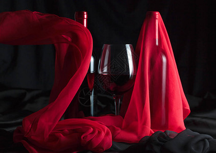 瓶子和一杯红酒黑色背景上的红色丝绸图片