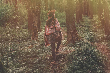 穿着帽子背包在绿色树林中行走的时装髦潮流女孩在夜图片