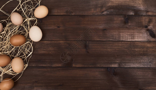 棕色新鲜鸡蛋和木制背景上的干草图片