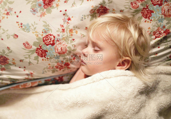 一个美丽的两岁幼儿正睡在花岗枕和白毛毯上图片