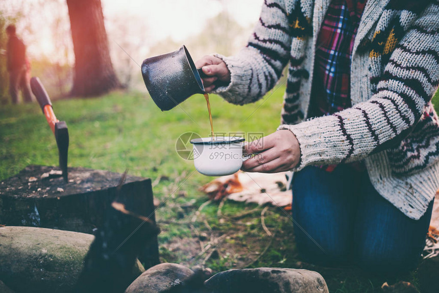 一个女孩在篝火旁喝咖啡一位女士正在准备着火的早晨咖啡布鲁内特把饮料倒进杯子里在森林里露图片