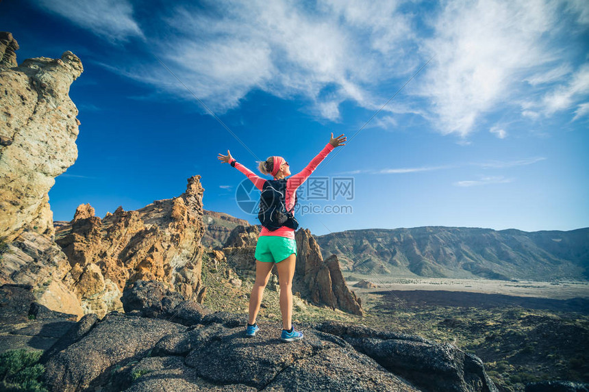 在山上张开双臂的女徒步旅行者达到了人生目标举起双手的女跑步者或登山者在西班牙加那利群岛特内里费岛的岩石小径上享受鼓图片