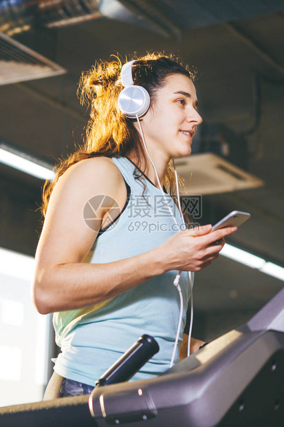 主题运动和音乐一个美丽的白种女人在跑步机上的健身房里跑步戴着大白耳机图片