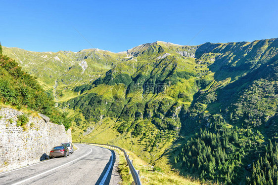 对弯曲的道路的日光视图与停放的汽车和背景上的绿色山脉明亮的蓝色晴朗的天空负拷贝空间图片