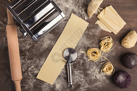生意大利面巢和面团切片与厨房桌子上的轮刀意大利面食配料和设备的顶视图片