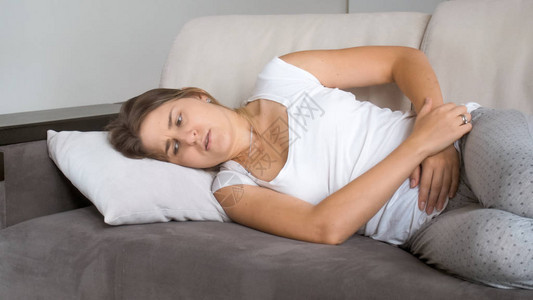 生病的女人躺在沙发上腹部疼痛图片