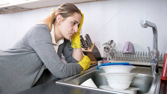 戴着手套看着满是脏盘子的厨房水槽的心烦意乱的家图片