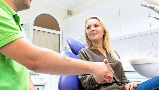 牙医与坐在牙医椅子上微笑的年轻女子握手的照片图片