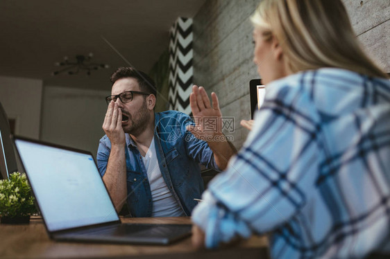 年轻劳累过度的商人坐在办公室打哈欠等待图片