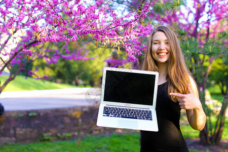 快乐的女孩在树旁展示笔记本电脑图片