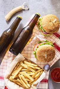 新鲜的美味汉堡薯条和两瓶啤酒在厨房毛巾上图片
