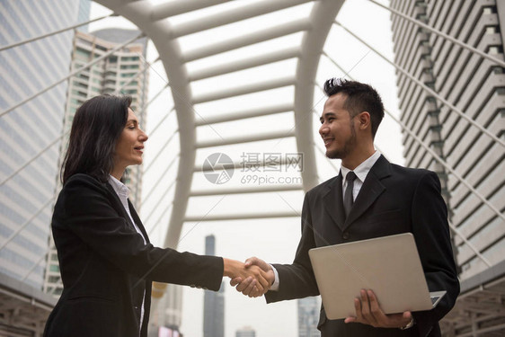 美国妇女和亚洲商人在完成项目协议后在现代城市握手在谈判之前尝试给合作伙伴留下第一印象成功的图片