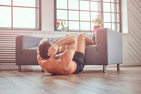 英俊的不穿衣服的肌肉男在家地板上做腹部运动图片