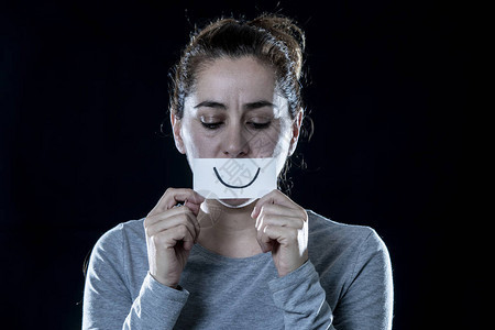 年轻美丽的悲伤和沮丧的拉丁女人用一张剪纸快乐的脸遮住她悲伤的脸图片