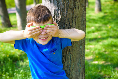在森林背景的太阳镜上微笑着可爱的小男孩用手闭上两只眼睛图片