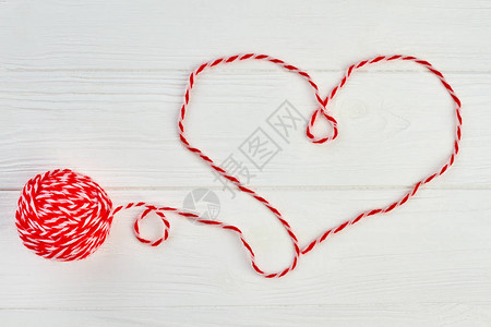 从红色羊毛线的心形状心由白色木制背景上的红色羊毛纱制成用于在木制背景上编织的毛球背景图片