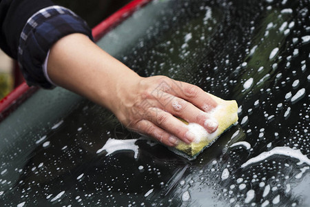 一名年轻的天主教女青年用海绵清洗一辆红色汽车的挡风图片