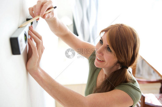 微笑的中年妇女用精神水平和铅笔在墙上打标记图片