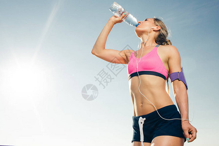青年运动女运动员在用智能手机耳从瓶子到蓝天使用臂带箱装饮用水时图片