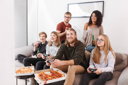 一群快乐的朋友在家里玩电子游戏吃披萨和喝啤图片