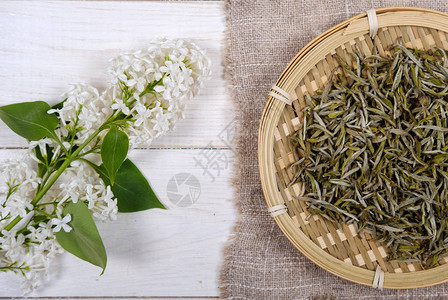 竹盘中的国白茶和木制背景上的白色丁香花图片