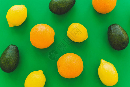 橙子鳄梨和柠檬在明亮的绿纸时尚背景上图片