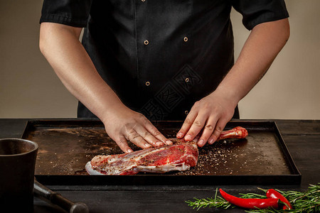 男厨师在木制餐桌上的石盘上用盐和胡椒来擦粗羊腿主厨为羊肉做开胃菜培训图片