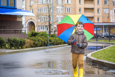小男孩在多雨的夏日公园玩耍带着五颜六色的彩虹伞防水外套和靴子的孩子在雨中跳进水坑和泥泞中孩子在秋季淋浴间散步任何天气都可以图片