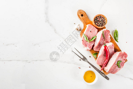 原生肉带香料的猪肉牛排草药橄榄油切割板上的白大理石背景顶视图片