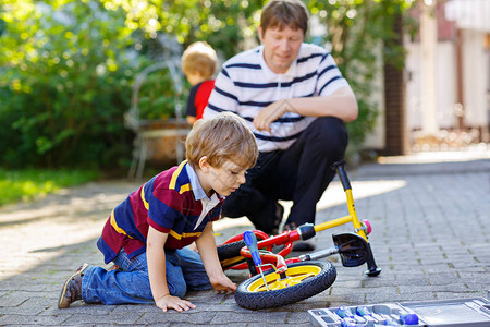 两个快乐的小男孩和父亲在自行车上修理链条并更换平衡自行车的轮子家庭与户外工作具一起工作积极休闲孩子图片