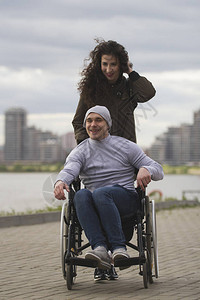 坐在轮椅上快乐的残疾男子与快乐的年轻女子一起在图片