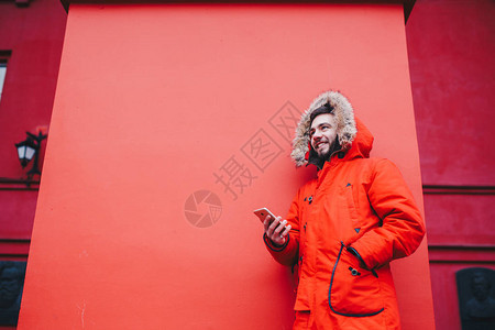 英俊的年轻男学生带着露齿的微笑和胡须站在红墙背景上背景图片