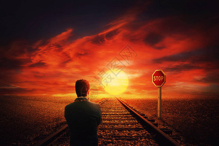 一个人在一条铁路上沿着沙漠在STOP路标前行走的超现实景象美丽的日落背景和商人思考他的下一步行动艰难的决定是图片