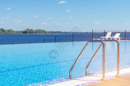 带楼梯和木甲板的游泳池在酒店蓝色游泳池里的扶手梯夏日阳图片